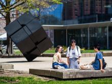 Three people talking on Regents Plaza, with the Cube and LSA building in the distance